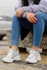 A person is sitting outdoors wearing jeans and sneakers. Produktbild-Vorschau