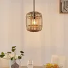 A hanging lamp made of rattan is shown above a dining table with a vase of plants and a glass of water. Produktbild-Vorschau