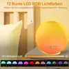 A bedside table with a sunrise alarm clock and a pillow in the background. Produktbild-Vorschau