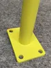 A close-up of a yellow metal base plate with a cylindrical pole attached, resting on a grey carpeted surface. Produktbild-Vorschau