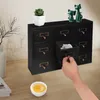 A hand is shown opening a drawer of a black wooden organizer with brass handles, placed on a wooden desk next to a small plant and decorative cat figurines. Podgląd zdjęcia produktu