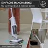 A person is using a Hoover vacuum cleaner and floor washer in a room with chairs. Produktbild-Vorschau