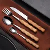 A set of cutlery with wooden handles is laid out on a brown cloth. Voir les images du produit