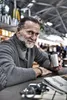 A man sits at a table with a newspaper and a cup. Anteprima dell’immagine prodotto