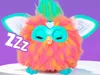 A colorful Furby toy is sleeping on a white surface against a purple background. Podgląd zdjęcia produktu