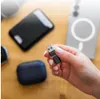 A hand holding a USB-C data blocker adapter with various electronic devices in the background. Produktbild-Vorschau