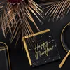 A New Year's Eve themed flat lay with black and gold napkins, a black plate, and gold palm leaves. Produktbild-Vorschau
