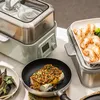 A kitchen scene featuring a multi-tier steamer, a frying pan with food, and a tray of cooked shrimp. Produktbild-Vorschau