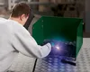 A person is welding inside a green welding booth. Produktbild-Vorschau