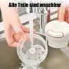 A person is rinsing a clear plastic food chopper with blades under a running faucet in a kitchen sink. A white and red food chopper lid is visible in the background. Produktbild-Vorschau
