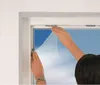 Hands installing a white mesh mosquito net onto a window frame. Náhled obrázku produktu