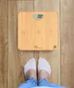 A person's feet wearing white socks stand on a wooden floor in front of a digital scale. Produktbild-Vorschau
