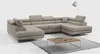 A beige sectional sofa is shown in a studio setting with a coffee table and a floor lamp. Produktbild-Vorschau