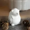 A white ceramic hedgehog figurine sits on a dark surface surrounded by pinecones. Produktbild-Vorschau