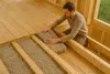 A man is installing insulation material between wooden beams in a room under construction. Anteprima dell’immagine prodotto