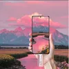 A hand holding a smartphone displaying a scenic landscape, with a pink river and mountains under a pink sky. Produktbild-Vorschau