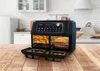 A black dual-chamber air fryer is shown on a wooden table in a kitchen setting. The air fryer has its doors open, revealing food inside. Produktbild-Vorschau