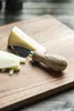 A cheese knife and pieces of cheese on a wooden cutting board. Produktbild-Vorschau