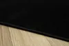 A close-up view of a black rug on a wooden floor. Voir les images du produit