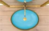 A top-down view of a light blue vessel sink with a gold rim and drain, mounted on a wooden wall. Náhľad obrázku produktu