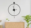 A modern black metal wall clock with a minimalist design hangs on a white wall above a wooden cabinet. Voir les images du produit