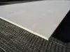 A close-up, angled view of a light-colored plywood sheet resting on a dark, textured surface. Produktbild-Vorschau