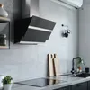 A modern kitchen scene featuring a black and silver range hood above a stovetop, with a sink and cutting boards in the background. Produktbild-Vorschau