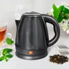A black electric kettle is shown on a white surface, with steam rising from its spout. A glass cup of tea, mint leaves, and tea bags are also visible. Produktbild-Vorschau