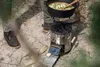 A person is cooking outdoors on a portable rocket stove. Produktbild-Vorschau