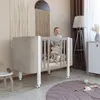 A baby is standing in a crib in a nursery room. Produktbild-Vorschau