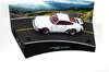 A white Porsche 911 Turbo model car is displayed on a diorama of a winding road with a mountain backdrop. Náhled obrázku produktu