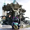 A black Maneki-Neko cat figurine sits in front of a large, ornate fountain. Produktbild-Vorschau