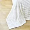 A white textured blanket is draped over a light wooden surface. Náhled obrázku produktu