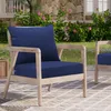 An outdoor chair with dark blue cushions sits on a patio next to a stone wall and flowering bushes. Produktbild-Vorschau