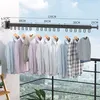 A wall-mounted retractable clothes drying rack with clothes hanging on it, set against a balcony with a city view. Produktbild-Vorschau