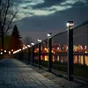 A pathway lined with a fence featuring solar-powered lights at dusk, with city lights reflected in the fence. Anteprima dell’immagine prodotto