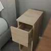 A narrow bedside table with one drawer pulled out, next to a bed. Produktbild-Vorschau