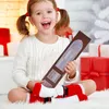 A young girl is sitting on a fluffy white rug, holding a brown advent calendar with mini books inside. She is wearing a white sweater and red and white Santa socks. The background is decorated with red and white gift boxes and a white Christmas tree. Náhled obrázku produktu