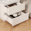 A white nightstand with two open drawers, showing a phone and headphones inside. Produktbild-Vorschau