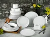 A collection of white dinnerware with black trim, arranged on a table with a chalkboard-style background and yellow flowers. Produktbild-Vorschau