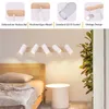 A bedroom scene with a wooden bed, a small white side table, and a wall-mounted light fixture with five white spotlights. The top part of the image shows close-ups of the product's features. Produktbild-Vorschau