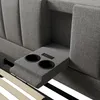 A close-up view of a gray upholstered bed frame, showing integrated cup holders and a control panel with USB and Type-C ports. Produktbild-Vorschau