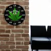 A round clock with a cannabis leaf design is displayed on a brick wall next to a black sofa. Produktbild-Vorschau
