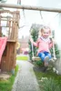 A young girl is happily swinging on a wooden swing set in a backyard. Produktbild-Vorschau