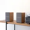 Two bookshelf speakers are placed on a wooden shelf next to some audio equipment. Produktbild-Vorschau
