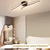 A modern ceiling lamp is shown in a bedroom setting, with a hand holding a smartphone displaying the same lamp. Voir les images du produit