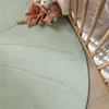 A close-up view of a green leaf-patterned rug next to a wooden crib with stuffed animals. Produktbild-Vorschau