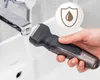 A hand holding a black and gray electric shaver under a running faucet in a white sink. Produktbild-Vorschau