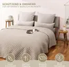 A bed with a beige quilted bedspread and pillows, with a cat sleeping on the bed. There are decorative icons at the bottom of the image. Anteprima dell’immagine prodotto