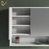 A white cabinet with open doors and shelves, against a dark green wall. A small jar is on one of the shelves. Produktbild-Vorschau